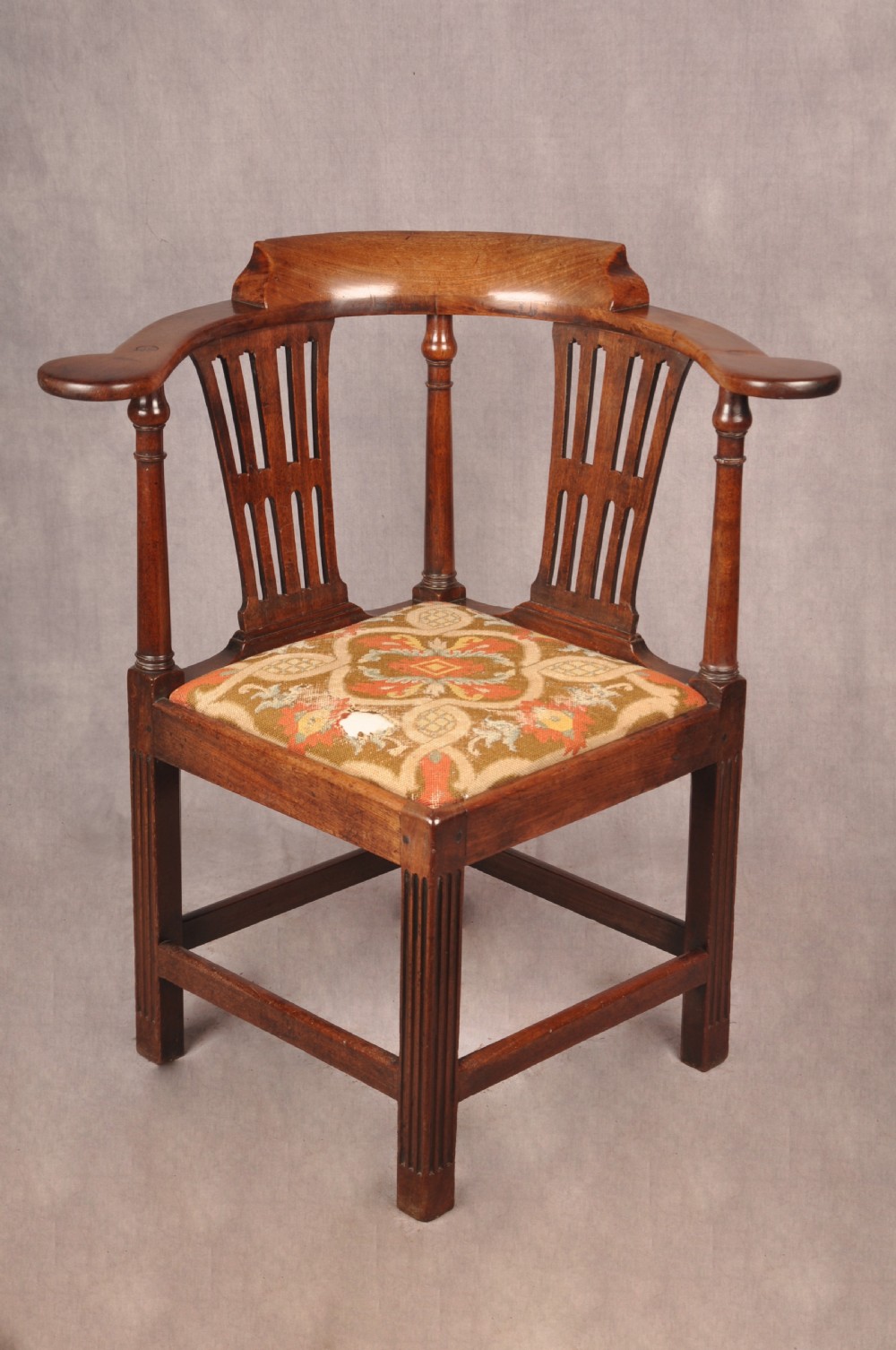 An 18th-century dark wood corner chair featuring a curved horseshoe backrest, dual pierced splats, turned uprights, fluted legs, and a patterned needlepoint drop-in seat.
