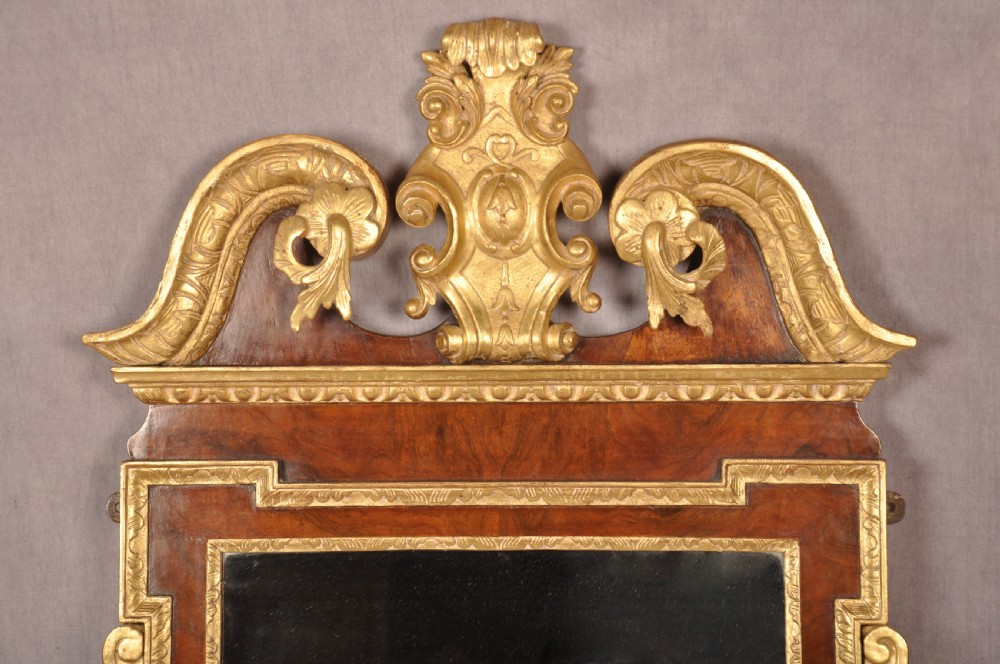 An 18th-century walnut and parcel gilt wall mirror featuring a carved swan-neck pediment, central cartouche crest, and floral side pendants. View III