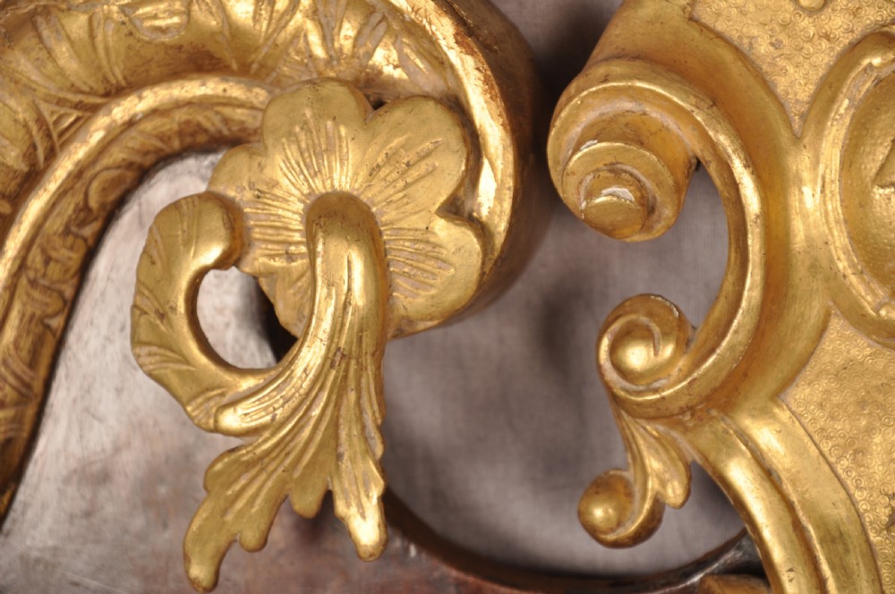 An 18th-century walnut and parcel gilt wall mirror featuring a carved swan-neck pediment, central cartouche crest, and floral side pendants. View V