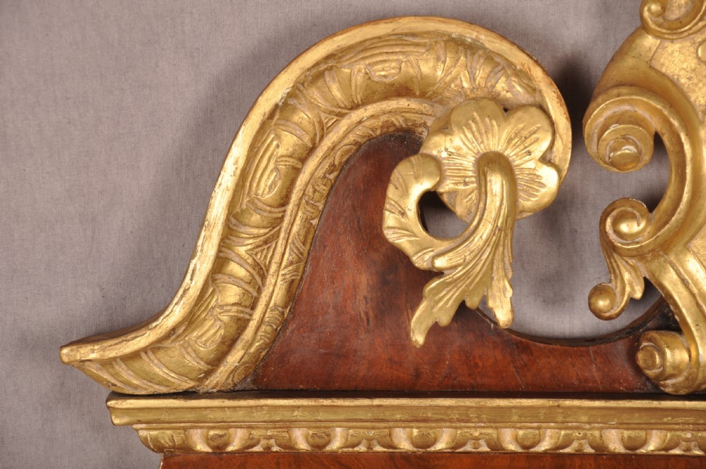 An 18th-century walnut and parcel gilt wall mirror featuring a carved swan-neck pediment, central cartouche crest, and floral side pendants. View VI