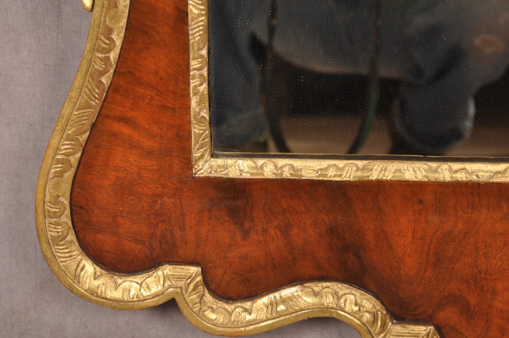 An 18th-century walnut and parcel gilt wall mirror featuring a carved swan-neck pediment, central cartouche crest, and floral side pendants. View IX