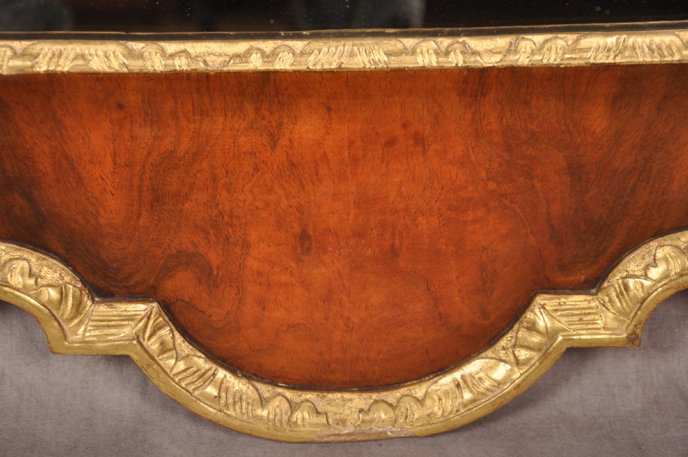 An 18th-century walnut and parcel gilt wall mirror featuring a carved swan-neck pediment, central cartouche crest, and floral side pendants. View X