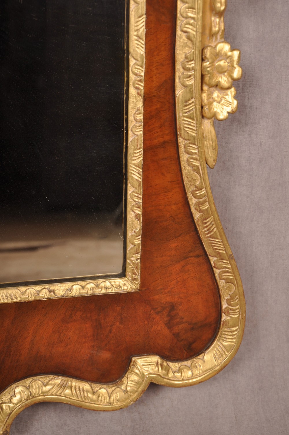 An 18th-century walnut and parcel gilt wall mirror featuring a carved swan-neck pediment, central cartouche crest, and floral side pendants. View XI