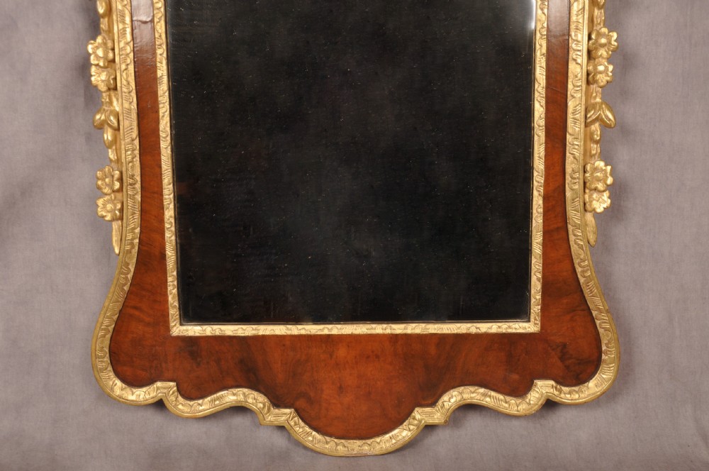 An 18th-century walnut and parcel gilt wall mirror featuring a carved swan-neck pediment, central cartouche crest, and floral side pendants. View XII