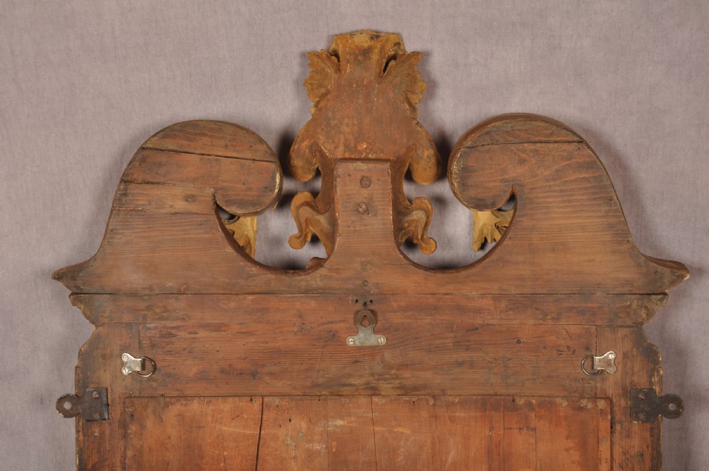 An 18th-century walnut and parcel gilt wall mirror featuring a carved swan-neck pediment, central cartouche crest, and floral side pendants. View XIV