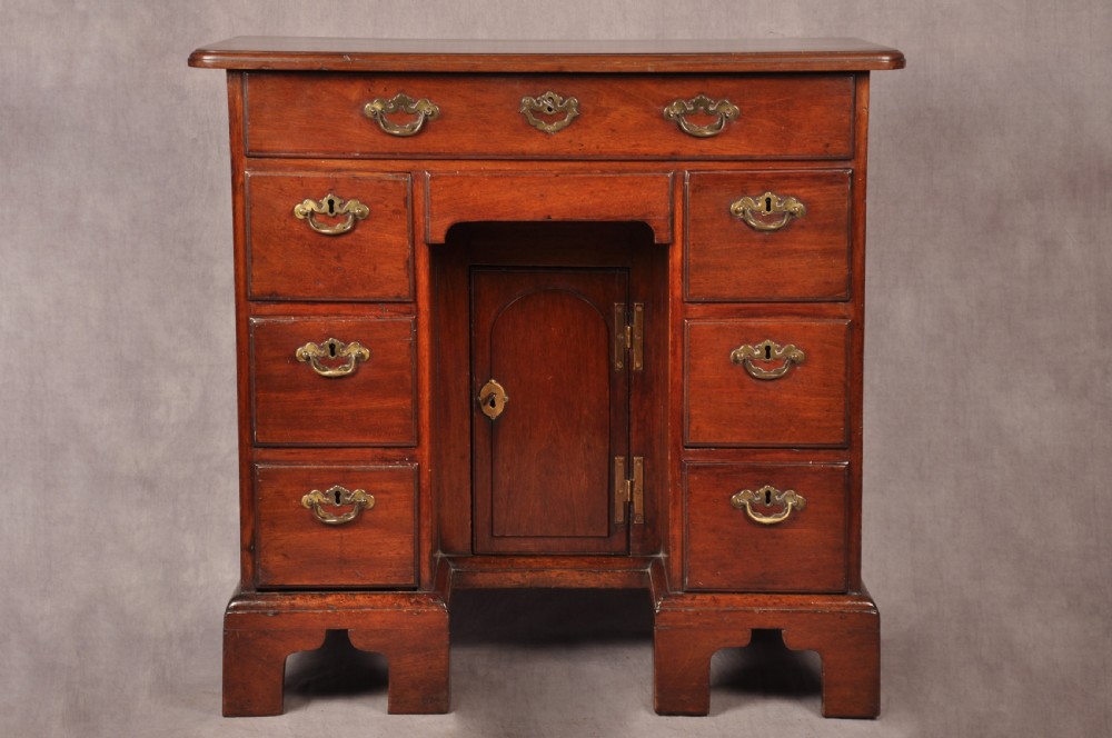 An 18th-century mahogany kneehole desk featuring multiple drawers with brass swan-neck handles, a central recessed cupboard, and bracket feet.