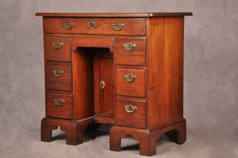 An 18th-century mahogany kneehole desk featuring multiple drawers with brass swan-neck handles, a central recessed cupboard, and bracket feet. View IV