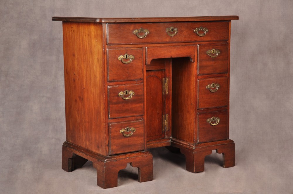 An 18th-century mahogany kneehole desk featuring multiple drawers with brass swan-neck handles, a central recessed cupboard, and bracket feet. View V