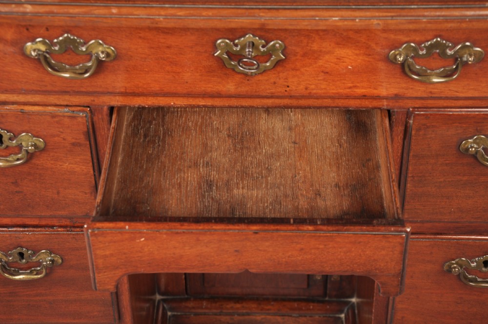 An 18th-century mahogany kneehole desk featuring multiple drawers with brass swan-neck handles, a central recessed cupboard, and bracket feet. View VI
