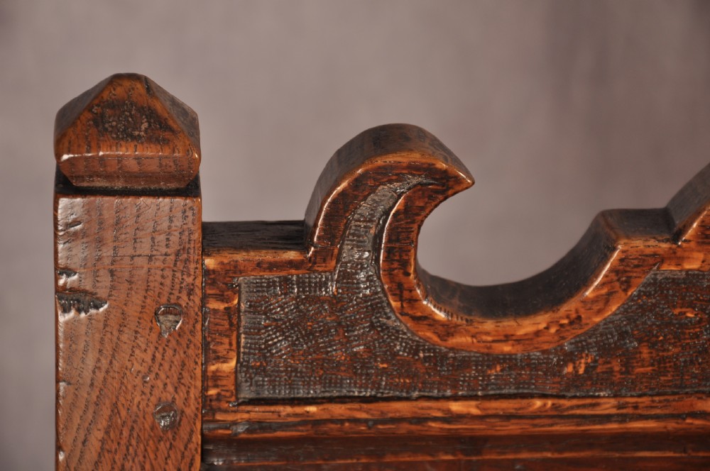 A pair of 17th century dark oak side chairs featuring carved crest rails, solid panel backs, and bobbin-turned front stretchers. View V