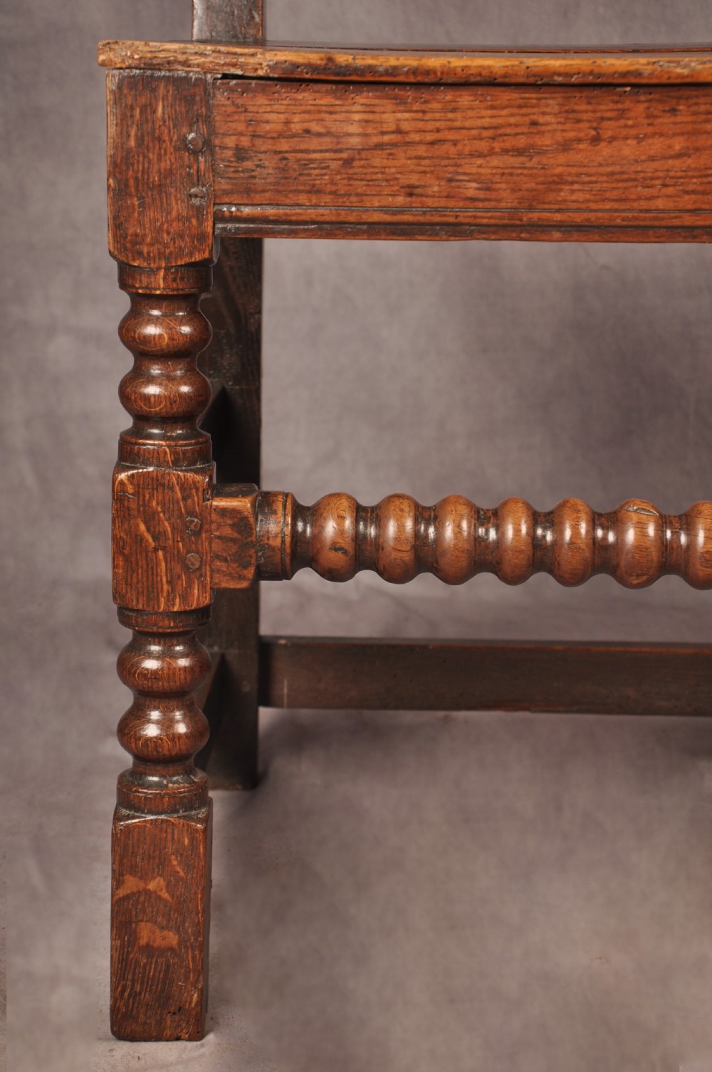 A pair of 17th century dark oak side chairs featuring carved crest rails, solid panel backs, and bobbin-turned front stretchers. View VII