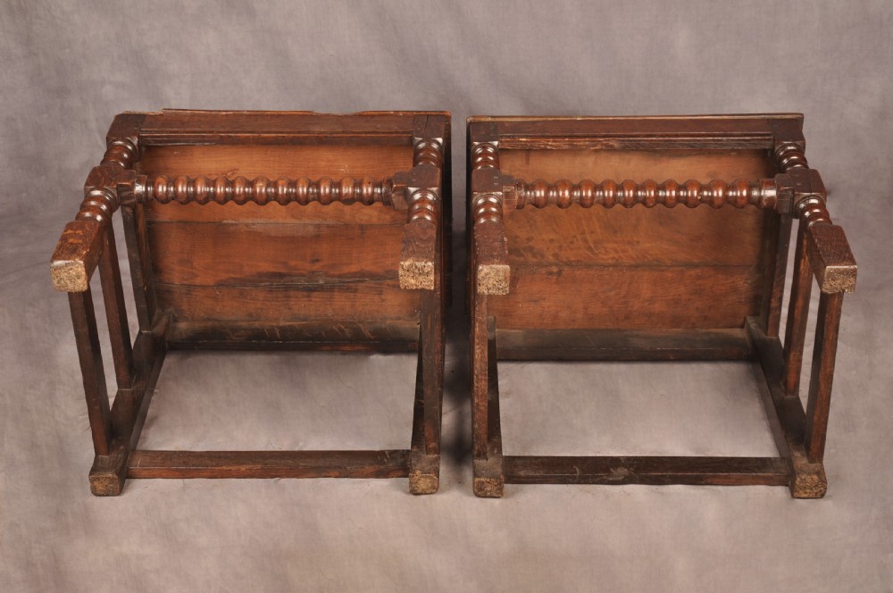 A pair of 17th century dark oak side chairs featuring carved crest rails, solid panel backs, and bobbin-turned front stretchers. View VIII