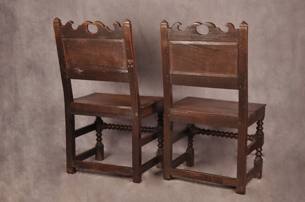 A pair of 17th century dark oak side chairs featuring carved crest rails, solid panel backs, and bobbin-turned front stretchers. View IX
