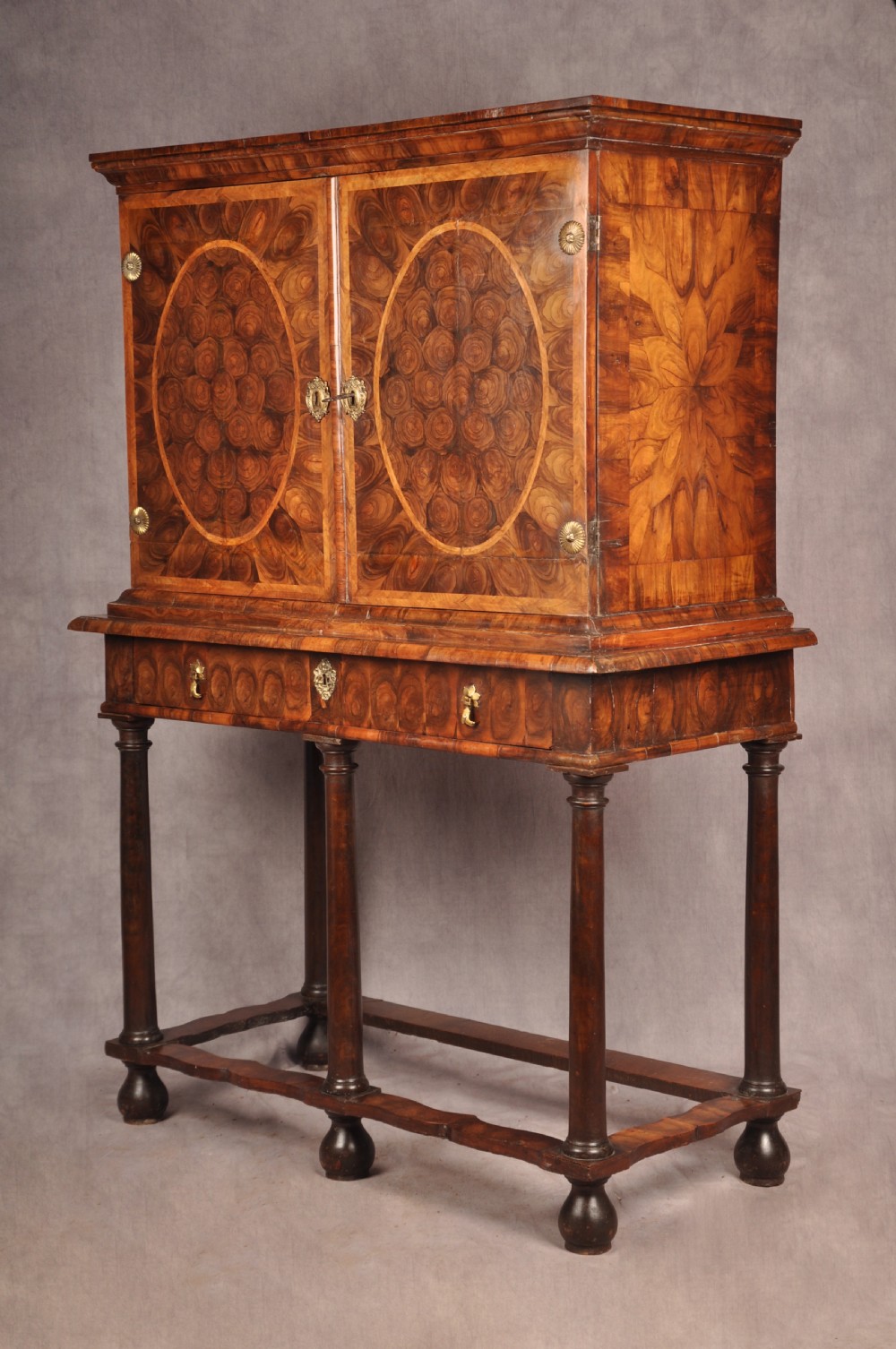 A 17th-century olive wood cabinet on stand featuring double doors inlaid with oval oyster veneer medallions, a lower drawer, turned legs, stretchers, and ball feet. View XXX