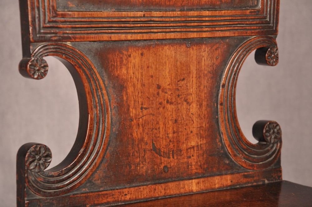A pair of antique dark mahogany Regency hall chairs featuring solid seats, turned front legs, and shaped backrests decorated with oval armorial crest medallions. View VII