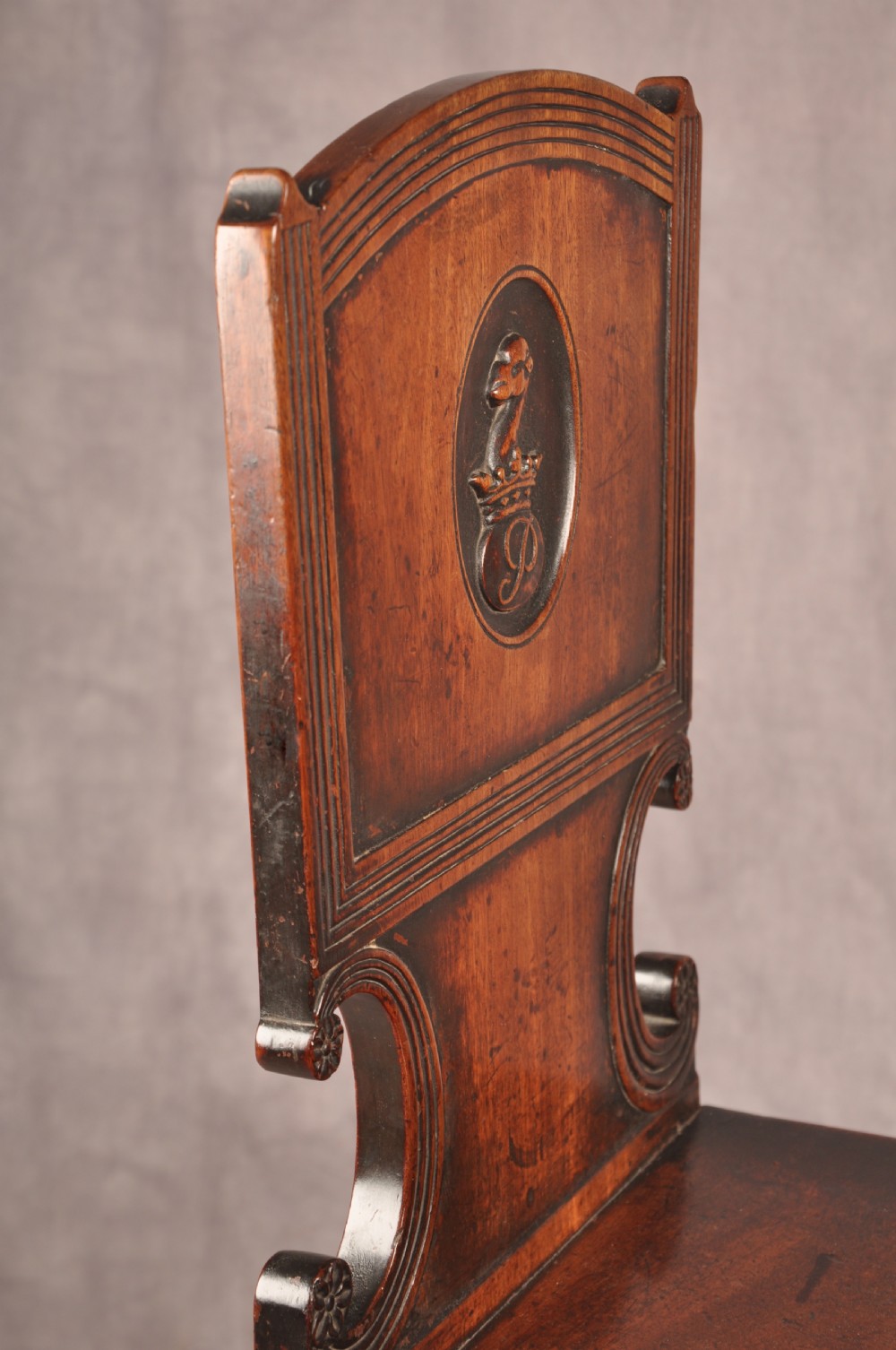 A pair of antique dark mahogany Regency hall chairs featuring solid seats, turned front legs, and shaped backrests decorated with oval armorial crest medallions. View VIII