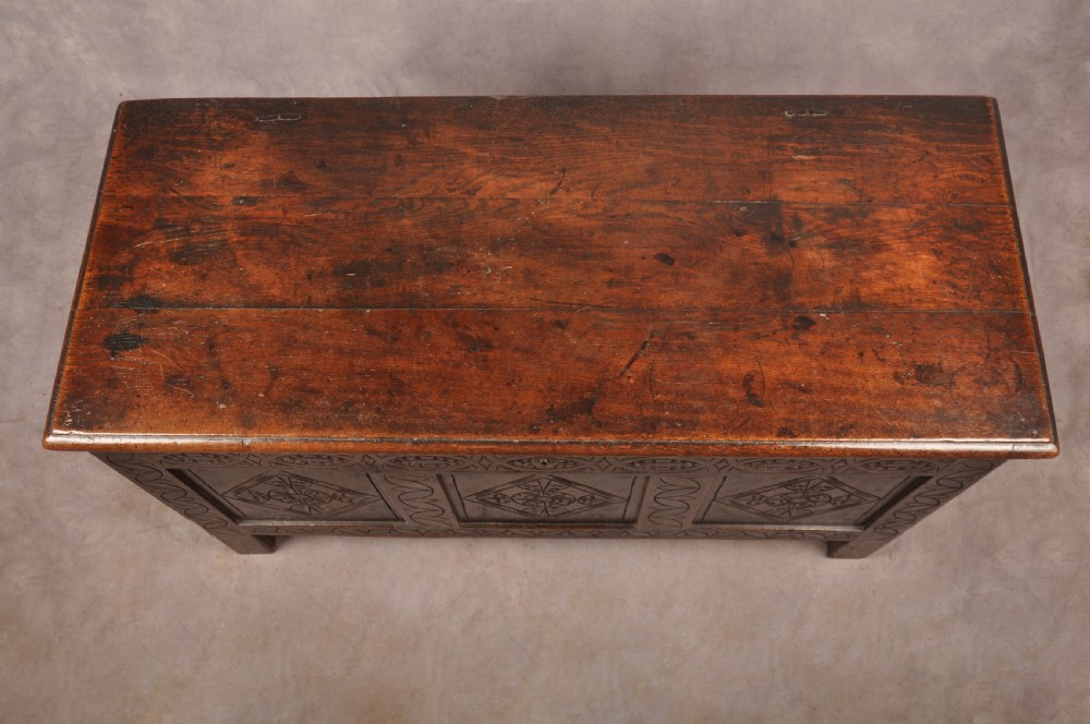 A 17th century carved oak coffer featuring three lozenge-carved front panels, leaf motifs, and ebonised detailing. View XVI