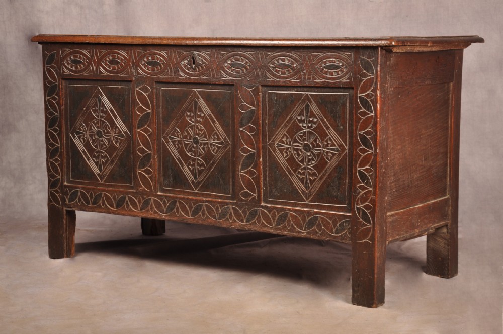 A 17th century carved oak coffer featuring three lozenge-carved front panels, leaf motifs, and ebonised detailing. View XVII