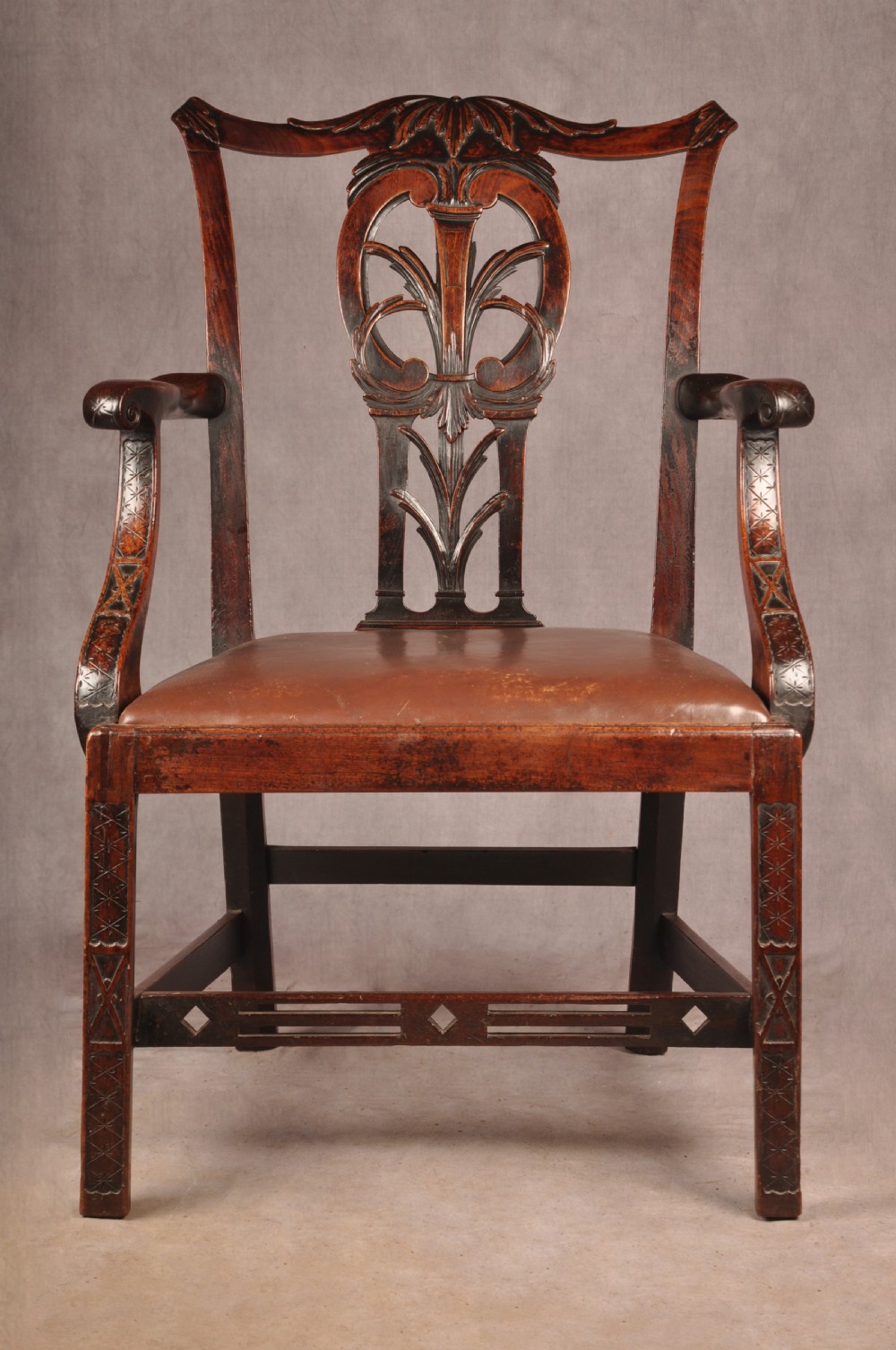 An 18th-century Chippendale carved mahogany armchair with a pierced splat, carved stretcher base, curved arms, and a warm brown leather seat.