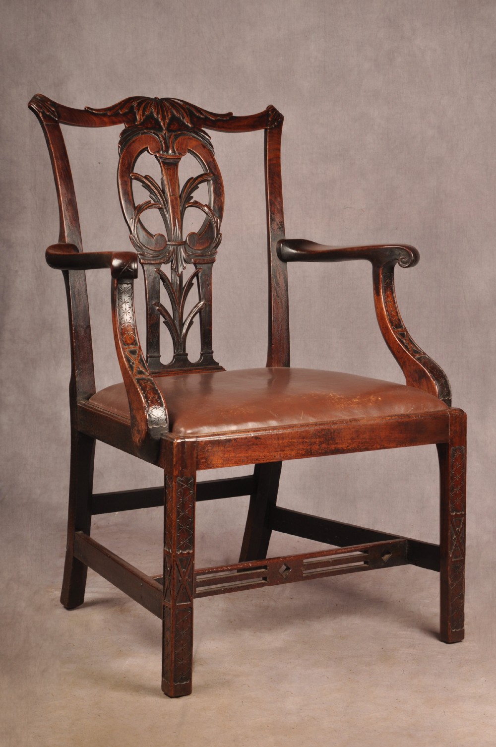 An 18th-century Chippendale carved mahogany armchair with a pierced splat, carved stretcher base, curved arms, and a warm brown leather seat. View VII