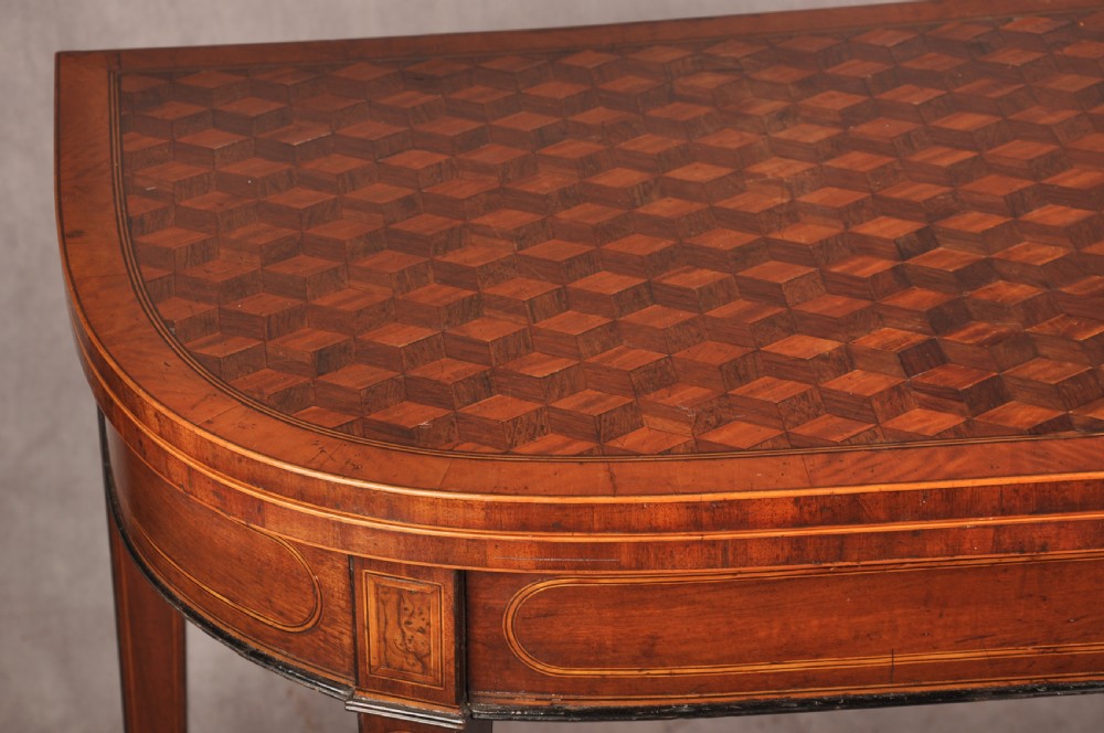 An 18th-century demilune card table featuring a geometric parquetry top, inlaid apron, and four square tapered legs ending in spade feet. View V