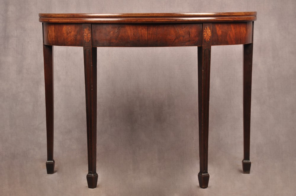 An 18th-century demilune mahogany tea table featuring tapered legs with inlaid patera motifs and spade feet.