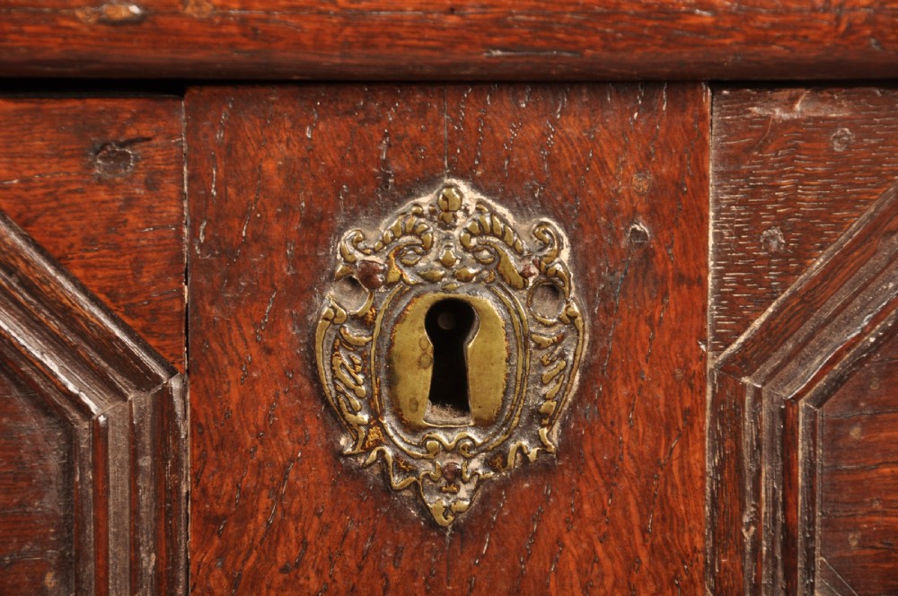 A Charles II dark oak chest of drawers featuring geometric moulded drawer panels, brass teardrop handles, keyhole escutcheons, and bun feet. View VI