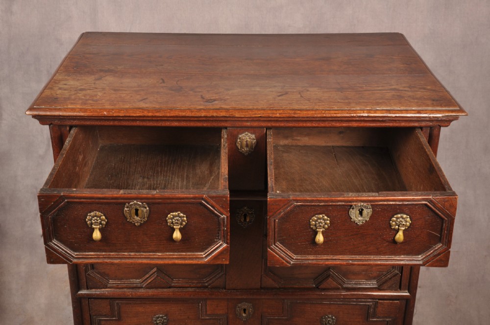 A Charles II dark oak chest of drawers featuring geometric moulded drawer panels, brass teardrop handles, keyhole escutcheons, and bun feet. View XII