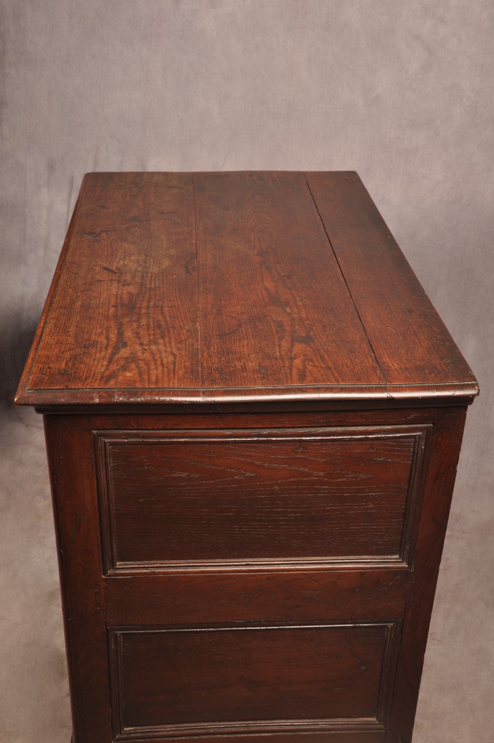 A Charles II dark oak chest of drawers featuring geometric moulded drawer panels, brass teardrop handles, keyhole escutcheons, and bun feet. View XVII