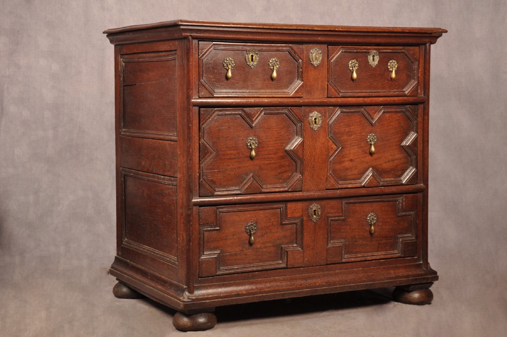A Charles II dark oak chest of drawers featuring geometric moulded drawer panels, brass teardrop handles, keyhole escutcheons, and bun feet. View XVIII