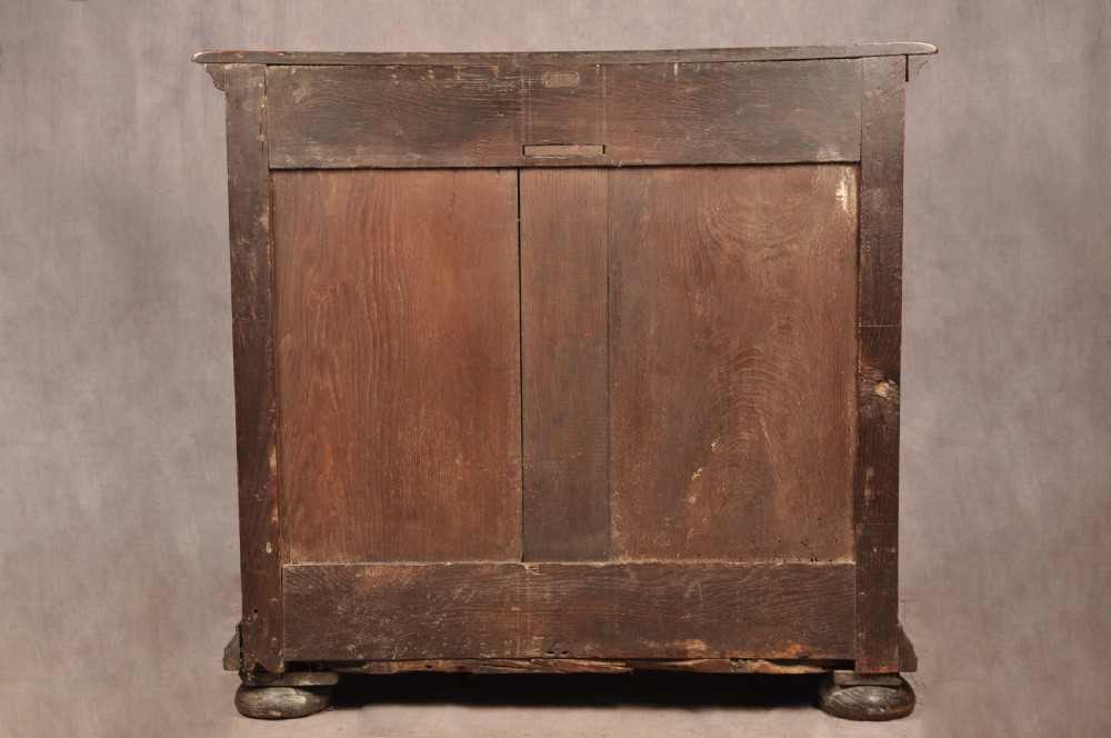 A Charles II dark oak chest of drawers featuring geometric moulded drawer panels, brass teardrop handles, keyhole escutcheons, and bun feet. View XX