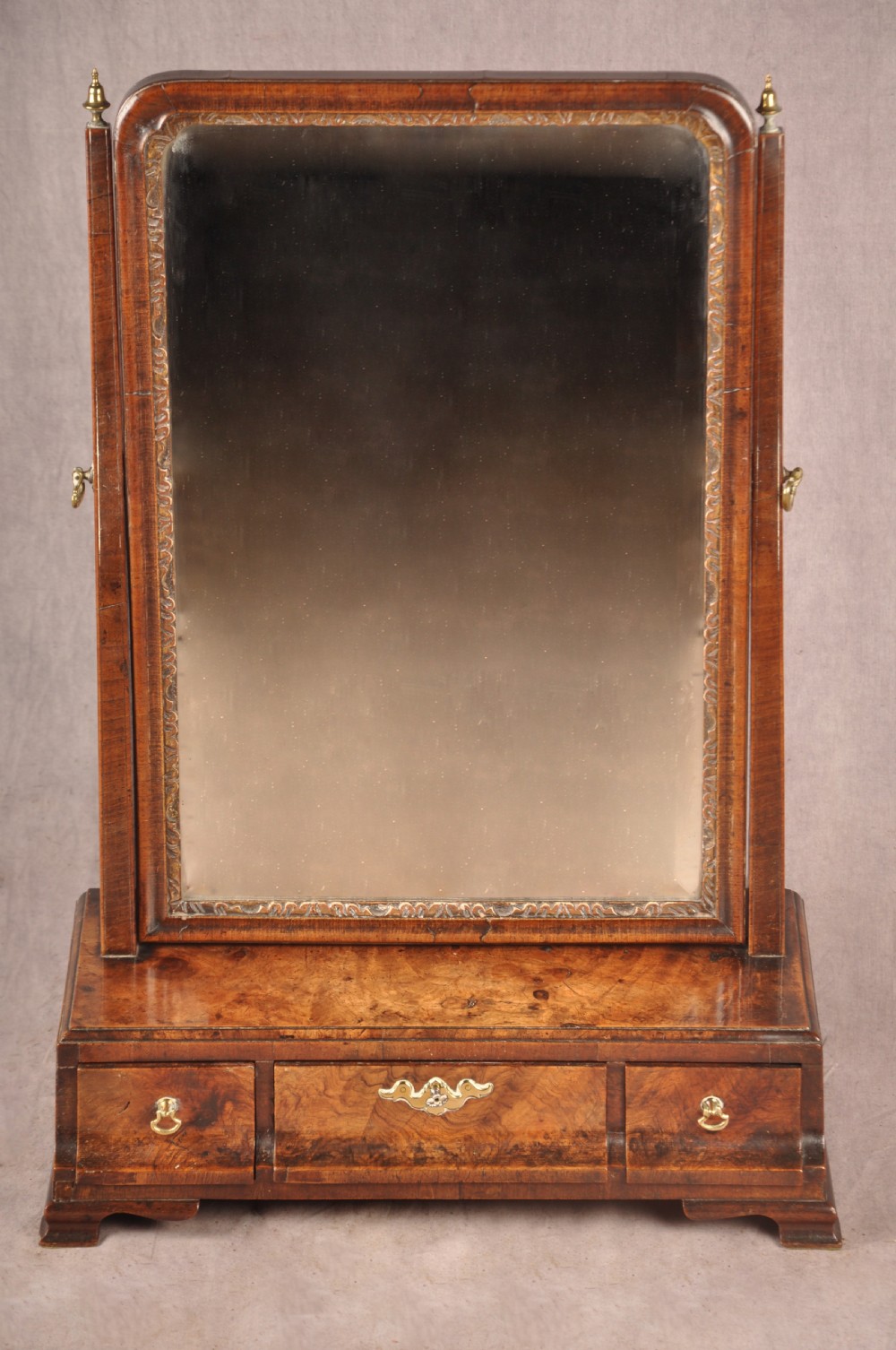 An 18th-century walnut toilet mirror featuring a rectangular adjustable glass frame resting above a three-drawer box base with brass handles.