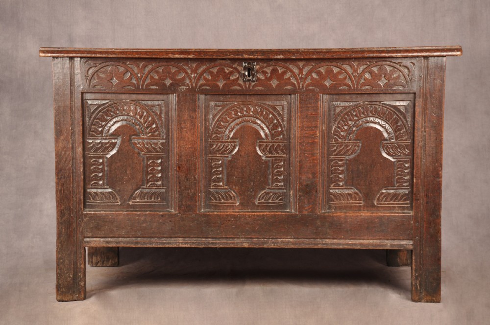 A 17th-century dark oak coffer with three carved arcaded front panels, an upper carved frieze, and a central iron lock plate.