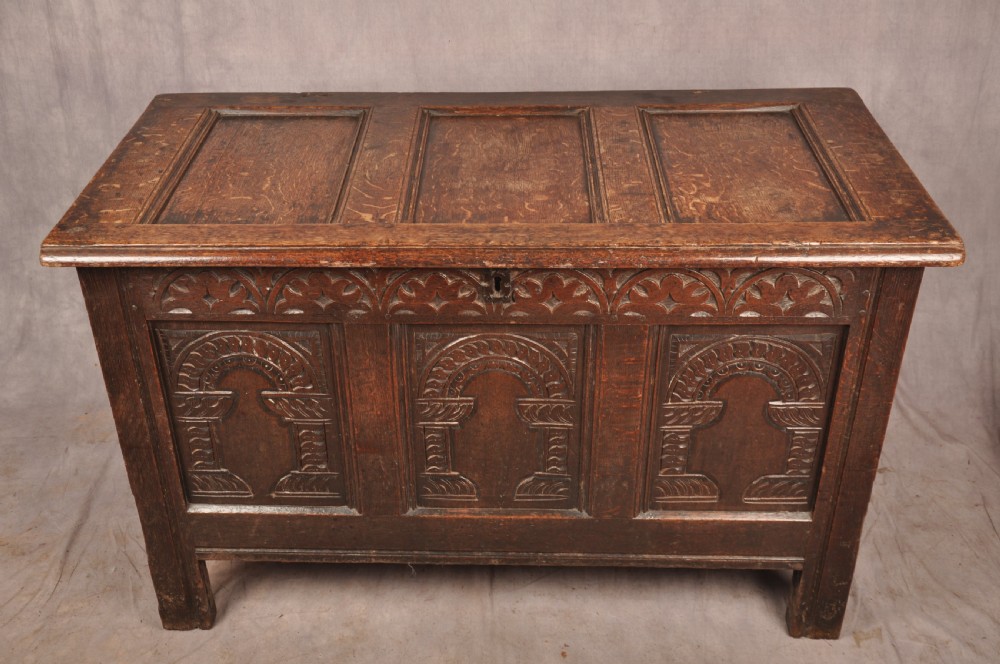 A 17th-century dark oak coffer with three carved arcaded front panels, an upper carved frieze, and a central iron lock plate. View V