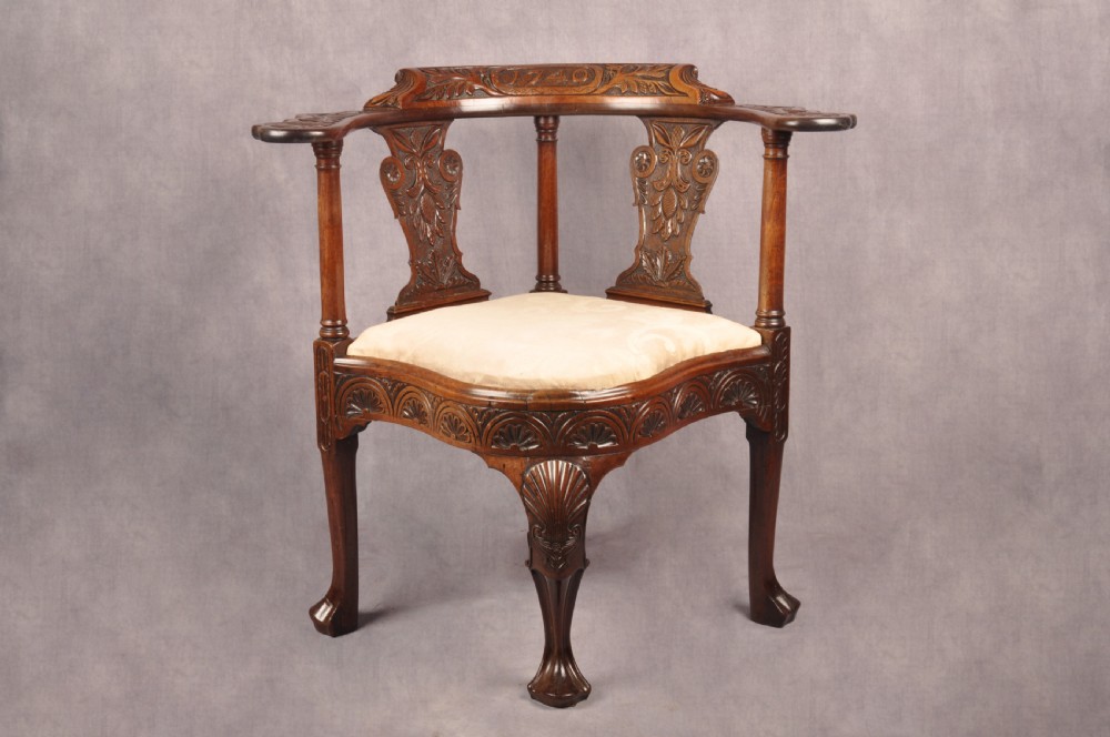 An 18th-century carved mahogany corner desk chair featuring detailed back splats, a shell-carved knee, cabriole legs, and a cream upholstered drop-in seat.
