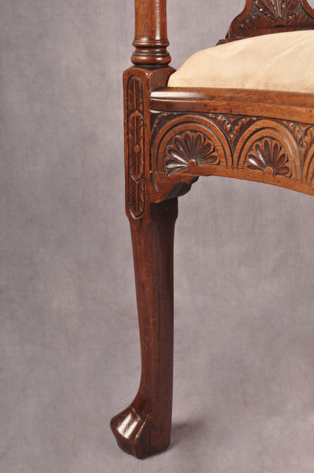 An 18th-century carved mahogany corner desk chair featuring detailed back splats, a shell-carved knee, cabriole legs, and a cream upholstered drop-in seat. View VI