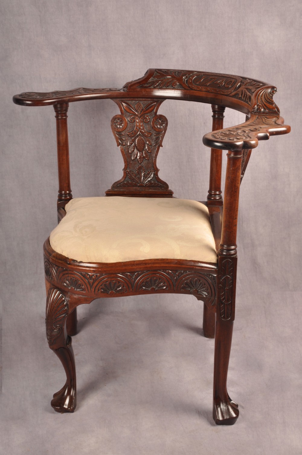 An 18th-century carved mahogany corner desk chair featuring detailed back splats, a shell-carved knee, cabriole legs, and a cream upholstered drop-in seat. View XIV