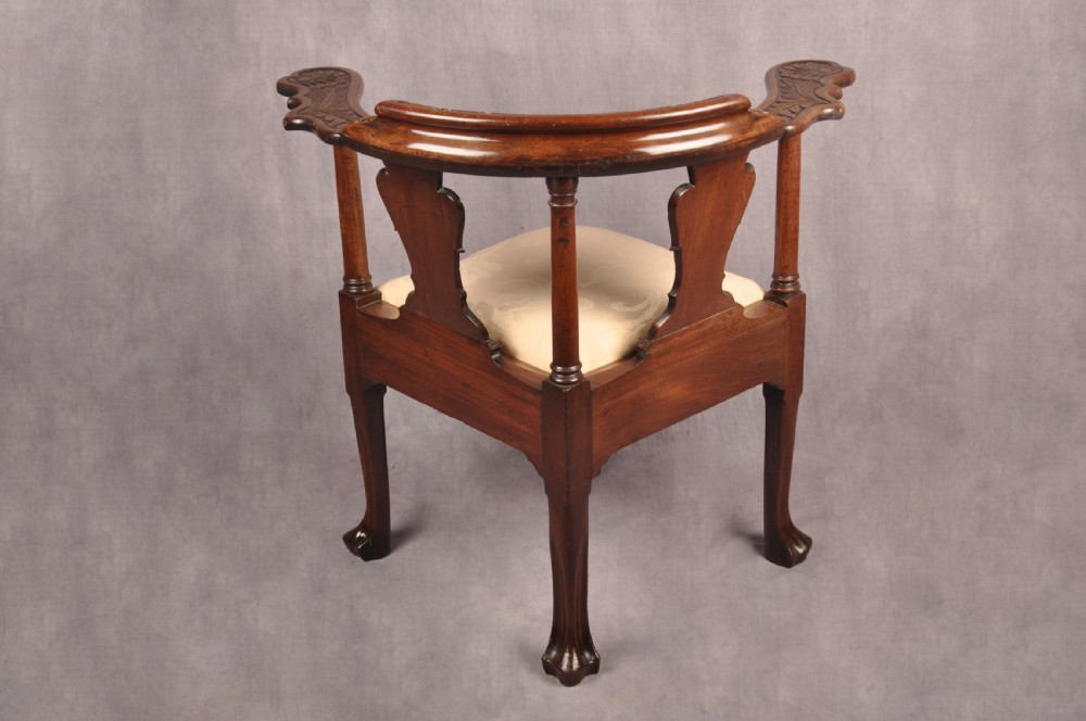 An 18th-century carved mahogany corner desk chair featuring detailed back splats, a shell-carved knee, cabriole legs, and a cream upholstered drop-in seat. View XVI
