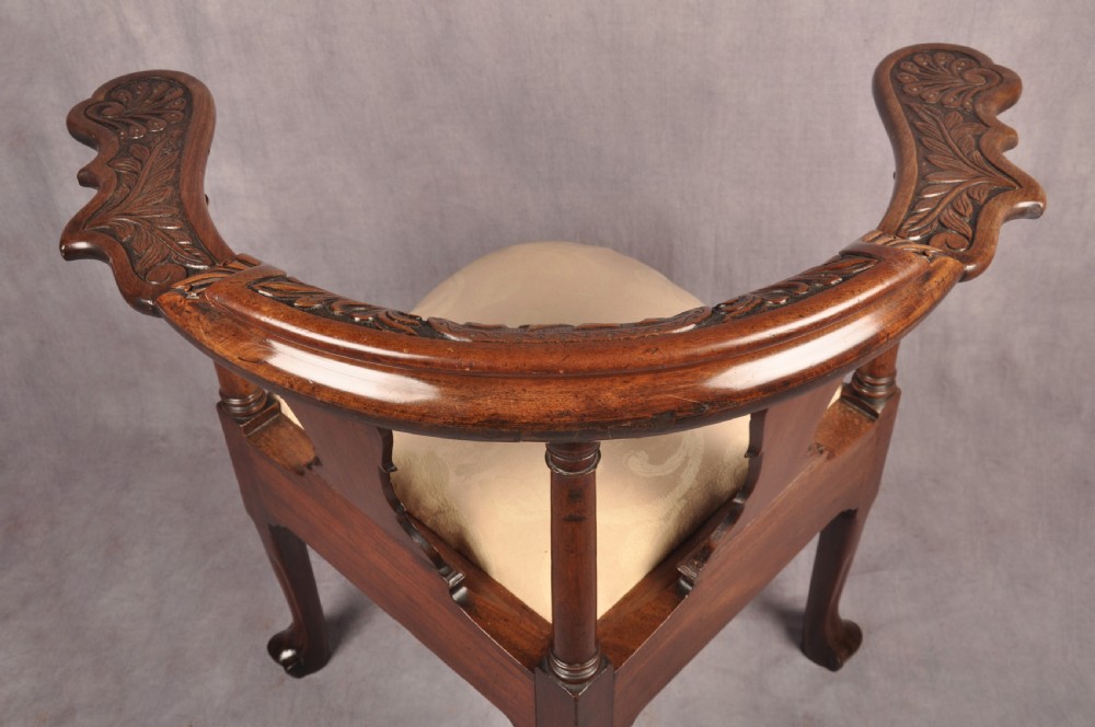 An 18th-century carved mahogany corner desk chair featuring detailed back splats, a shell-carved knee, cabriole legs, and a cream upholstered drop-in seat. View XVII