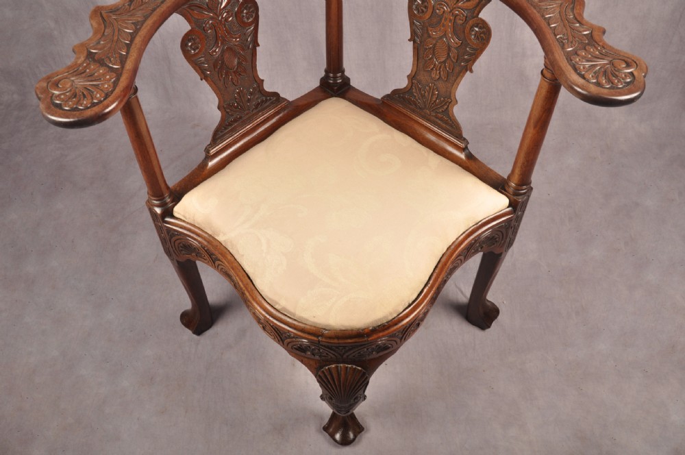 An 18th-century carved mahogany corner desk chair featuring detailed back splats, a shell-carved knee, cabriole legs, and a cream upholstered drop-in seat. View XVIII