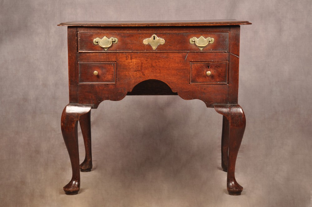 An early 18th-century dark walnut lowboy side table featuring cabriole legs with pad feet, three brass-handled drawers, and a shaped apron.