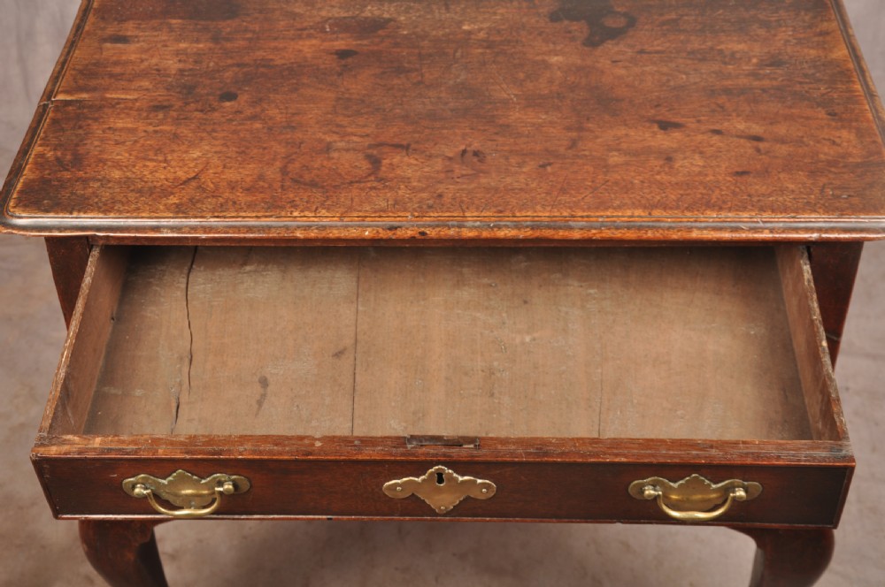 An early 18th-century dark walnut lowboy side table featuring cabriole legs with pad feet, three brass-handled drawers, and a shaped apron. View VI