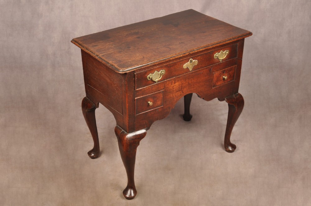 An early 18th-century dark walnut lowboy side table featuring cabriole legs with pad feet, three brass-handled drawers, and a shaped apron. View XII