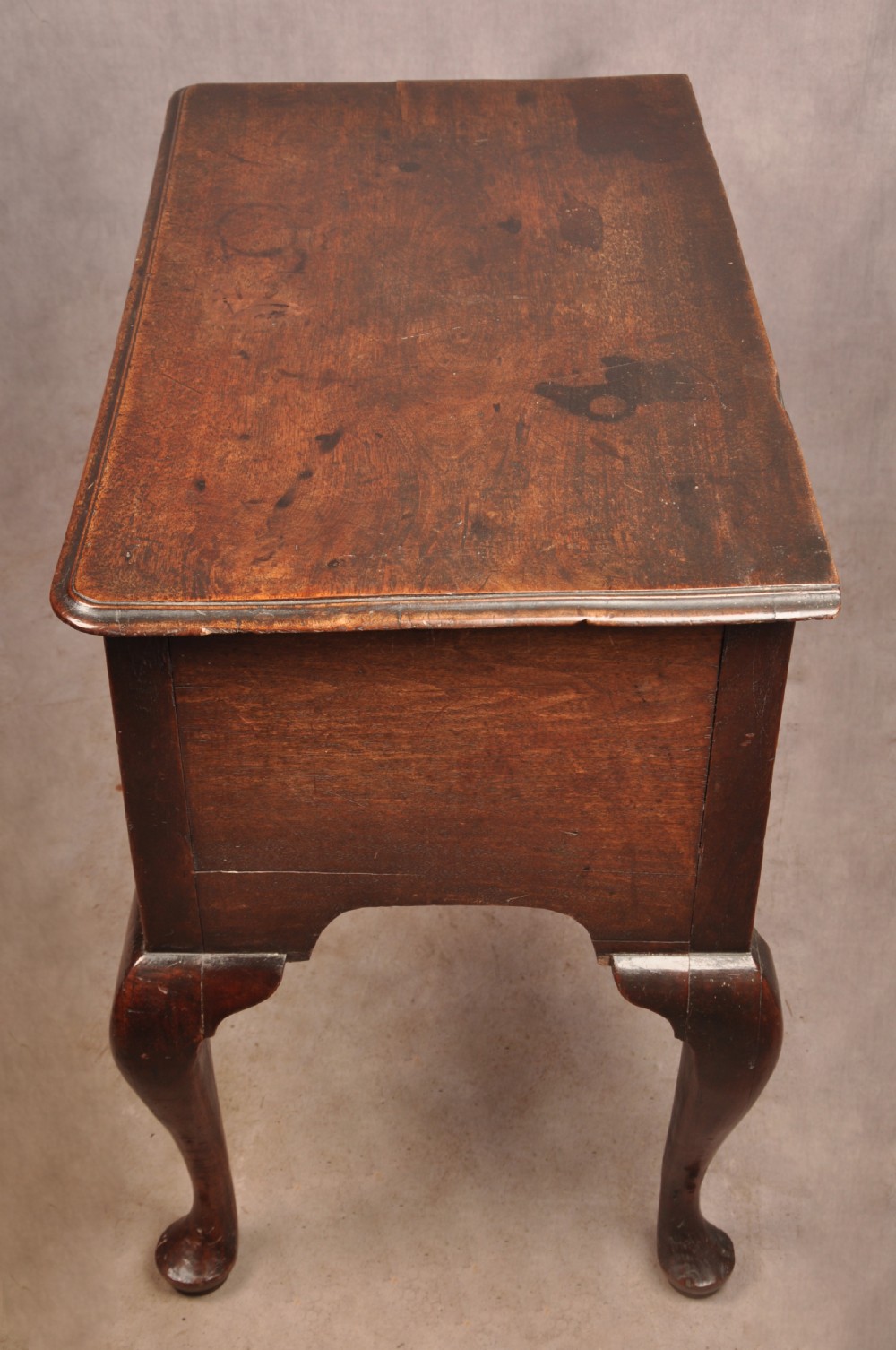 An early 18th-century dark walnut lowboy side table featuring cabriole legs with pad feet, three brass-handled drawers, and a shaped apron. View XIV