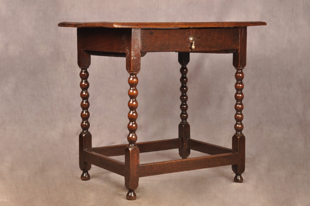 A dark oak 17th-century side table featuring four bobbin-turned legs, a lower box stretcher, and a single drawer with a teardrop brass pull.