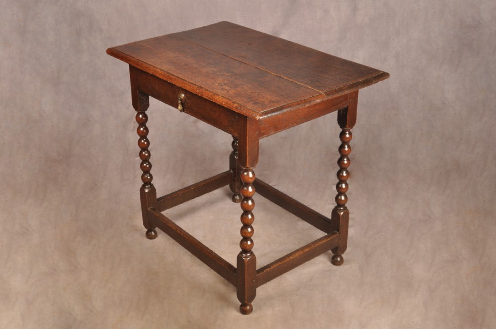 A dark oak 17th-century side table featuring four bobbin-turned legs, a lower box stretcher, and a single drawer with a teardrop brass pull. View II