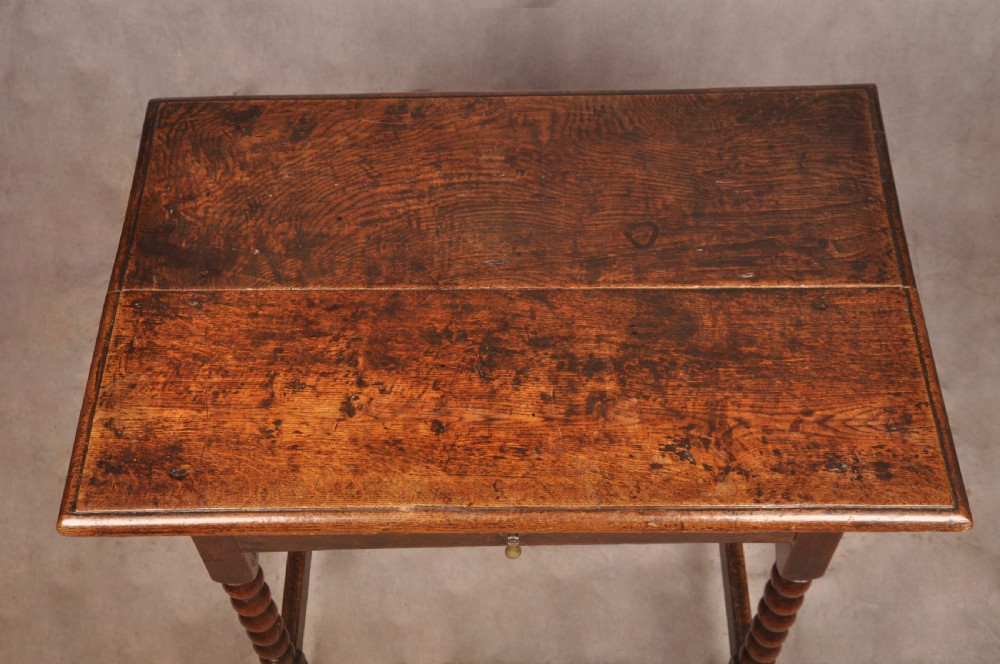 A dark oak 17th-century side table featuring four bobbin-turned legs, a lower box stretcher, and a single drawer with a teardrop brass pull. View III