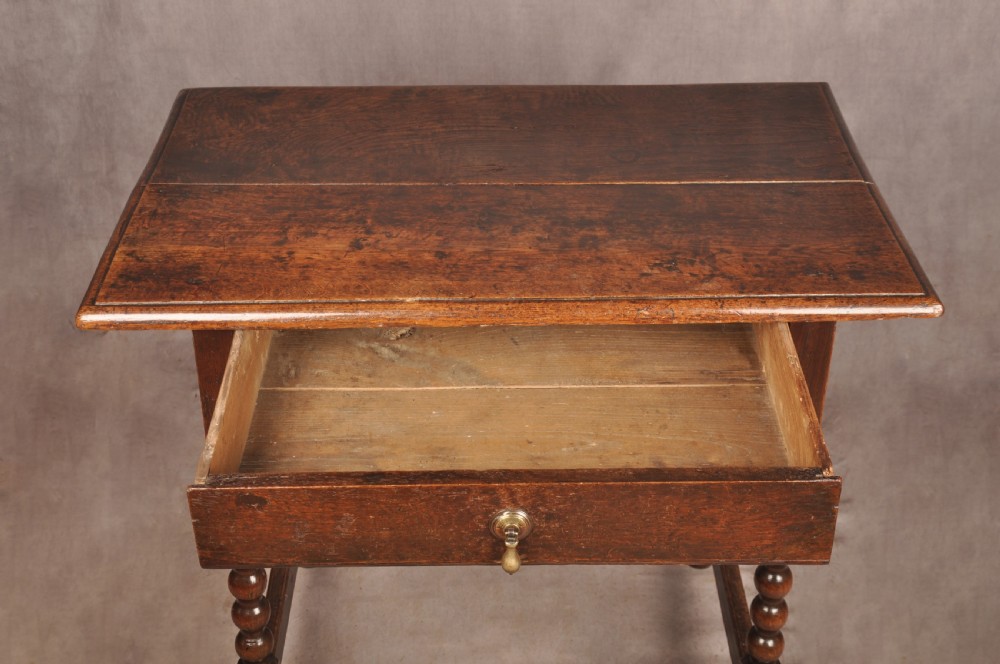 A dark oak 17th-century side table featuring four bobbin-turned legs, a lower box stretcher, and a single drawer with a teardrop brass pull. View IV