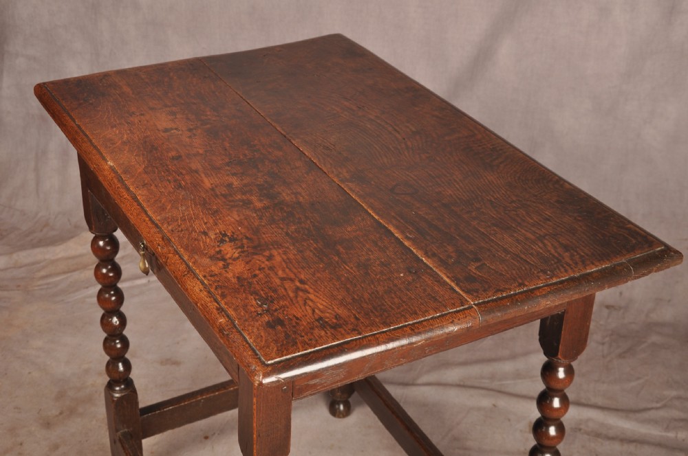 A dark oak 17th-century side table featuring four bobbin-turned legs, a lower box stretcher, and a single drawer with a teardrop brass pull. View VI