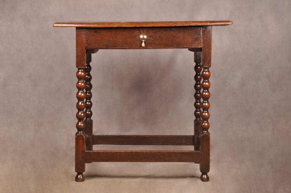 A dark oak 17th-century side table featuring four bobbin-turned legs, a lower box stretcher, and a single drawer with a teardrop brass pull. View VII